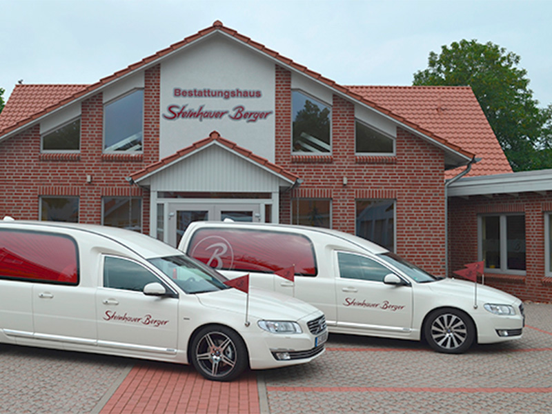 Zwei weiße Bestattungsfahrzeuge der Berger GmbH in Lüneburg vor modernem Backsteingebäude, repräsentativ für professionelle und würdevolle Bestattung.