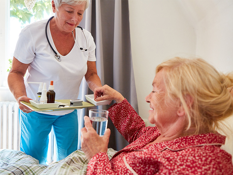 Pflegefachkraft bringt eingehende Medikamente ans Bett einer Seniorin – zeigt liebevolle häusliche Krankenpflege in Ebstorf.