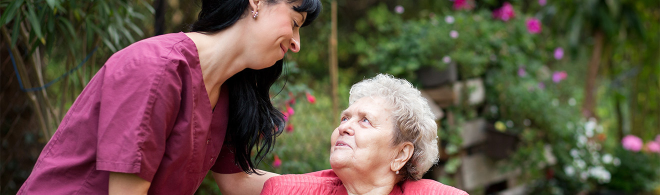 Pflegekraft begleitet Seniorin im grünen Garten, beide lächeln und genießen fürsorgliche häusliche Krankenpflege in Ebstorf.