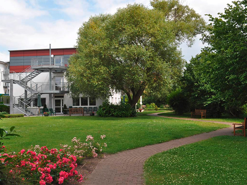 Großzügiger Gartenbereich der Birkenhof Senioren- & Pflegepension in Salzwedel mit gepflegter Rasenfläche, Gehweg und Bäumen – ideal für Spaziergänge und Erholung